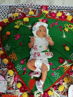 a baby laying on top of a green and red blanket with flowers around it's head