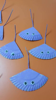 four blue paper plates with eyes hanging from them on an orange table top, one is shaped like a fish and the other has two are made out of cardboard