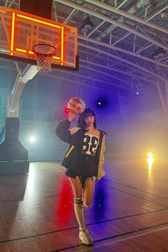 a woman standing on top of a basketball court holding a basketball in her hand with the hoop above her head