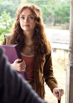 a woman holding a binder in her hand and talking to another person with an umbrella