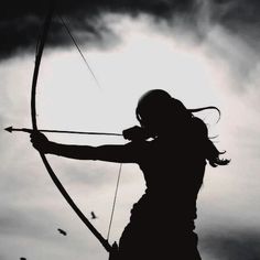 the silhouette of a woman holding a bow and arrow in front of a cloudy sky