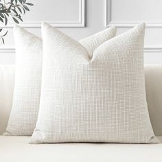 two white pillows sitting on top of a couch next to a potted olive tree