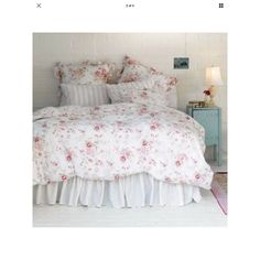 a white bed with pink flowers on the comforter and pillow cases in a bedroom