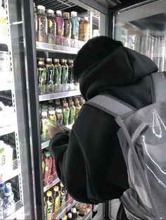 a person with a back pack looking at drinks in a refrigerator