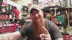 a man with a long beard gives the thumbs up sign in a shop filled with tools