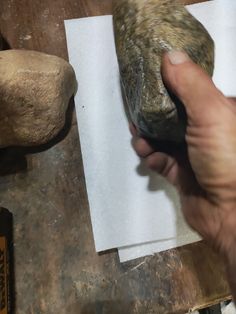 a person is holding something in their hand near some rocks and paper on the table