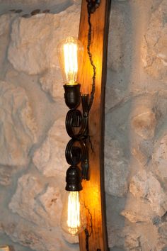 a wooden light fixture with two lights on it's side and a stone wall in the background