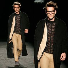 a male model walking down the runway wearing glasses and a black coat with an overcoat