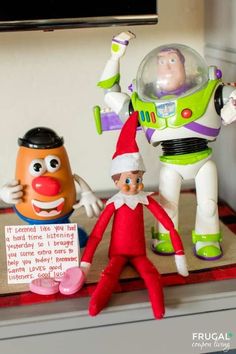 an elf is standing next to two toy characters on a table with a sign in front of him