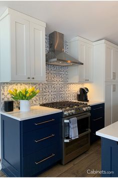 a kitchen with blue cabinets and white counter tops, yellow flowers in a vase on the stove