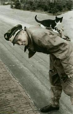 a man with a cat on his back standing next to a street and looking at the ground