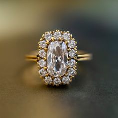 an oval shaped diamond surrounded by smaller round diamonds on a gold band, sits atop a shiny surface