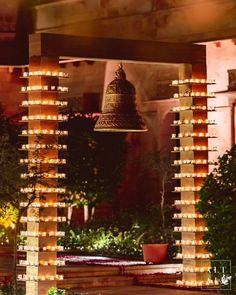 a bell hanging from the side of a building next to trees and plants with lights on them