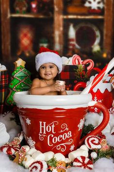 a baby sitting in a hot cocoa cup surrounded by christmas decorations and candy canes