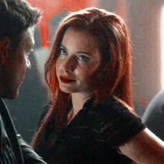 a woman with red hair is talking to a man