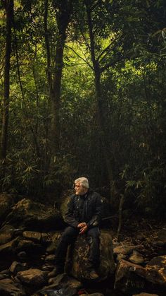 a man sitting on top of a rock in the forest