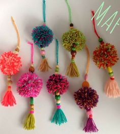 the colorful pom poms are hanging from strings on the white wall, which says may