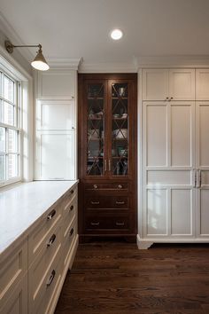 an empty kitchen with white cabinets and wood flooring, along with a large window