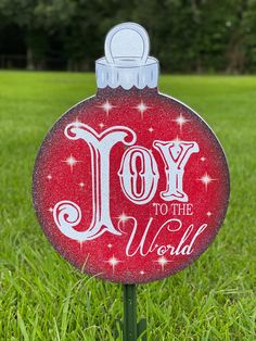 a red ornament with the words joy to the world on it sitting in grass