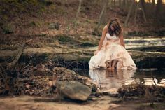 a woman in a white dress is standing in the water and looking down at her shoes