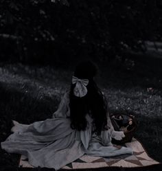 a woman with long hair sitting on a blanket in the grass wearing a white dress