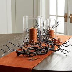 two candles are sitting on a table with branches