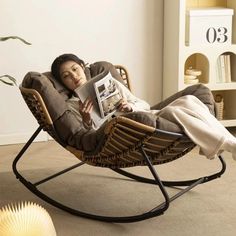 a woman laying in a rocking chair reading a magazine