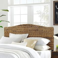 a wicker headboard with white linens and pillows on a bed in front of a window