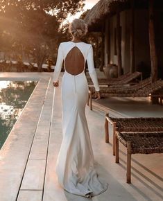 a woman in a long white dress is walking towards the pool with her back to the camera