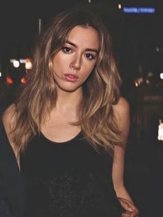 a beautiful young woman standing in front of a building at night with her hand on her hip