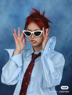 a woman with red hair wearing sunglasses and a tie holding her hands up in the air