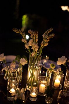 a table topped with lots of candles and vases filled with flowers on top of it