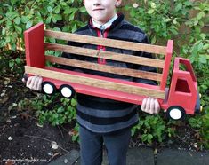 a young boy holding up a wooden toy truck