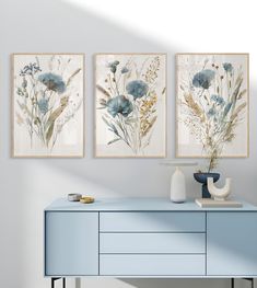 three paintings on the wall above a blue dresser with vases and other decor items