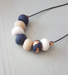 a necklace made out of different colored beads on a black cord with a gold and white bead