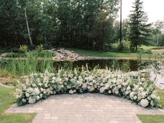 an outdoor wedding ceremony with white flowers and greenery on the ground near a pond