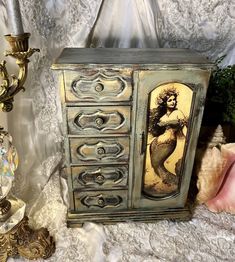 an old fashion jewelry box with a mermaid painting on the front and sides, next to a candle holder