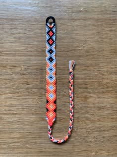 an orange, blue and white lanyard with a black hook on a wooden surface