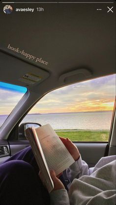 someone is reading a book in the back seat of a car while looking out at the ocean