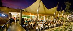 a group of people sitting at tables under umbrellas in front of an outdoor restaurant