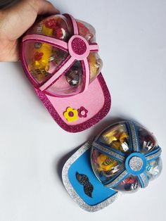 a hand is holding a pink and blue toy car next to a plastic case filled with assorted toys