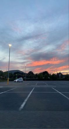 an empty parking lot at dusk with the sun setting in the distance and clouds covering the sky