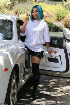 a woman with blue hair standing next to a white car and giving the peace sign