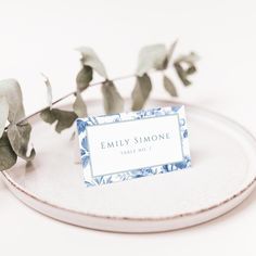 a place card sitting on top of a white plate next to a leafy branch