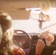 a woman sitting in the driver's seat of a car holding a bouquet of flowers