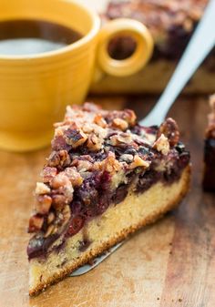 a slice of blueberry coffee cake on a wooden cutting board next to a cup of coffee