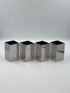 four silver square vases are lined up on a white surface, with one in the middle