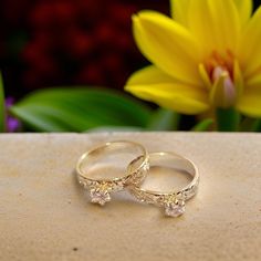 two gold wedding rings sitting on top of a stone slab next to a yellow flower