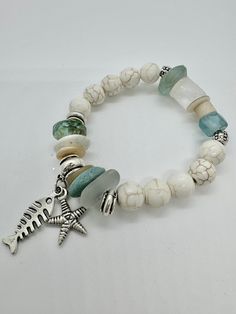 This unique "Coastal Charm: Handcrafted Cream Howlite, Raw Quartz, African Recycled Glass, and Czech Glass Beaded Bracelet with Antiqued Silver Accents and Sea Life Charms" is a stunning blend of natural gemstones and mixed beads, creating a one-of-a-kind piece that complements any outfit. The antiqued silver accents and sea life charms add a touch of coastal elegance, making it a perfect accessory for any occasion. Each bead is carefully selected and handcrafted with attention to detail, ensuri White Bohemian Czech Glass Bracelets, Bohemian White Czech Glass Bracelets, Handmade White Czech Glass Bracelets, Czech Glass Bead Bracelet, Glass Beaded Bracelet, Coastal Elegance, Quartz Gemstones, Recycled Glass Bead, Beach Bracelets