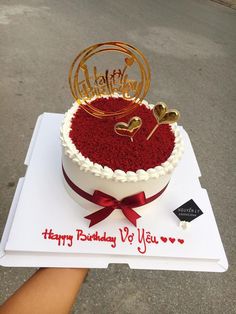 a happy birthday cake with red velvet and gold decorations on top is held up by someone's hand